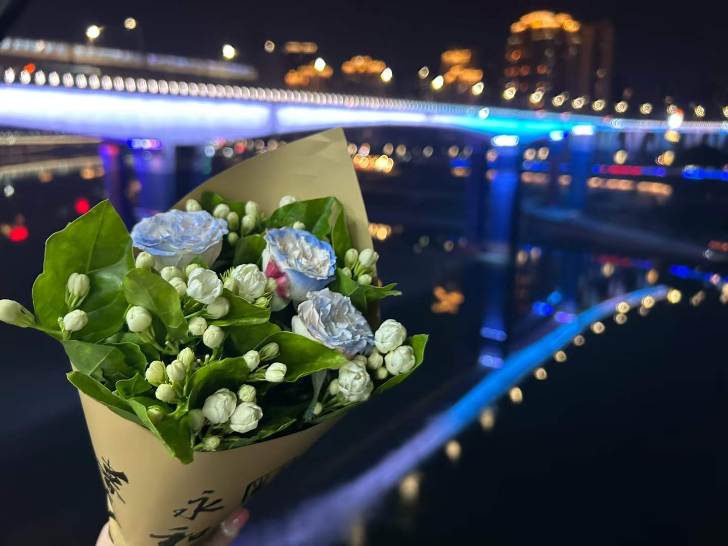 江边的花束，背景是亮起蓝色灯光的桥